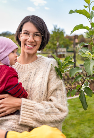 Woman with child in her arms in front of an apple tree